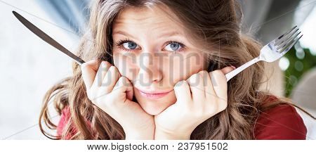 Portrait Of Hungry Woman With Fork And Knife In Hands. She Is Waiting For Food In A Cafe