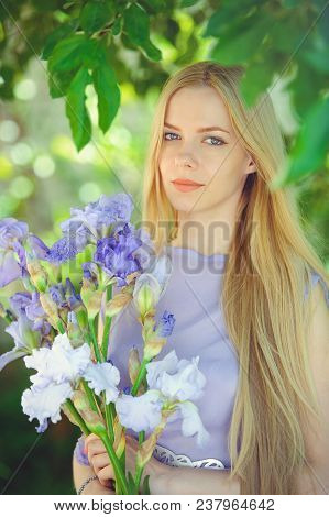 Attractive Young Girl With Blonde Dren Hair And Natural Make-up Smelling Blue Purple Iris Flowers On