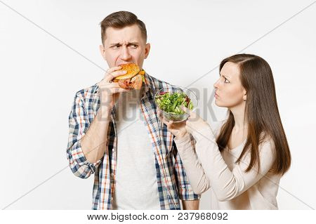Fun Young Couple, Man And Woman Standing With Green Fresh Salad In Glass Bowl, Eating Burger Isolate