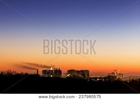 Cityscape With Dramatic Sky  Sunset. Silhouette Of Buildings And Smoking Pipes. Urban Industrial Cit