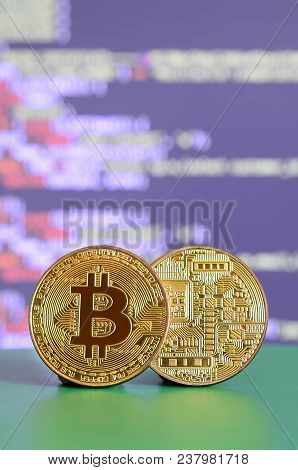 Two Gold Bitcoins Lie On The Green Surface On The Background Of The Display, Which Shows The Process