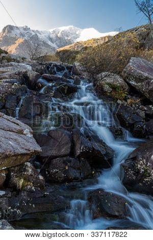 Early Morning Light And Shadow Over Mountains And Snow. Glyder Farw. Waterfall On Stream. Landscape