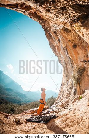 Climber Prepares To Climb The Route. A Man Looks At A Rock. Preparation For Training. Climbing On Na