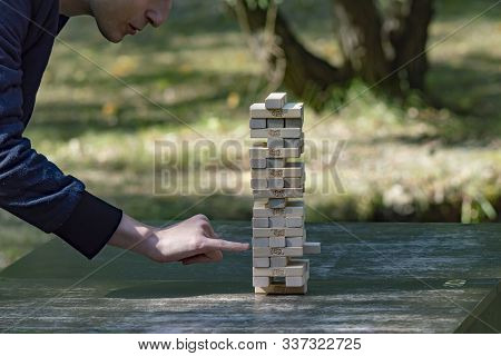 Guy Sticks Out Wooden Block From  Tower Of Game Jenga. Side View. Concept. Surgut, Russia - Septembe