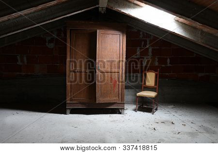 Old Wooden Wardrobe And A Vintage Chair In The Dusty Attic Without People
