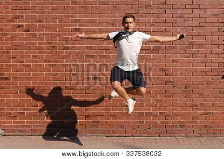 Young Man In White T-shirt Jump With Crosed Hands, Spread His Arms Wide And Looking At The Camera, R