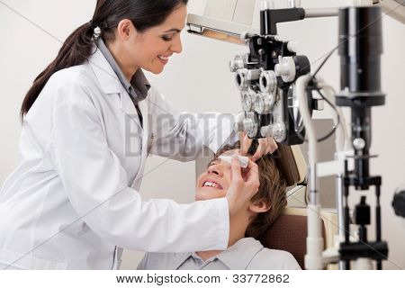 Optometrista giovane sorridente mettendo occhio gocce negli occhi del paziente per una visione chiara