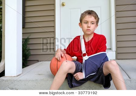 Garçon avec le bras en écharpe assis avec un ballon de basket