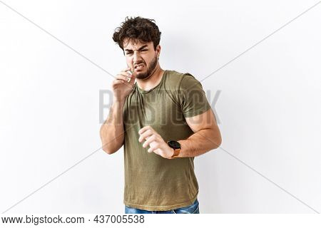 Hispanic man standing over isolated white background disgusted expression, displeased and fearful doing disgust face because aversion reaction. 
