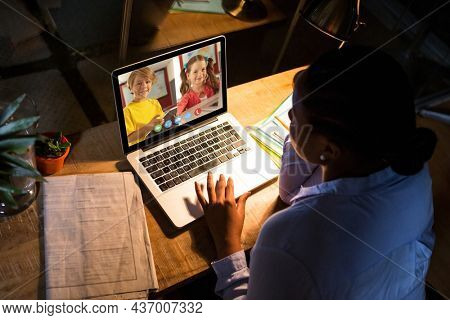 African american woman using laptop for video call, with diverse elementary school pupils on screen. communication technology and online education, digital composite image.
