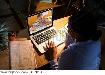 African american woman using laptop for video call, with elementary school pupil on screen. communication technology and online education, digital composite image.