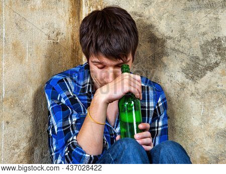 Sad Young Man With A Beer Bottle In Alcohol Addiction In The Corner Of Old Wall