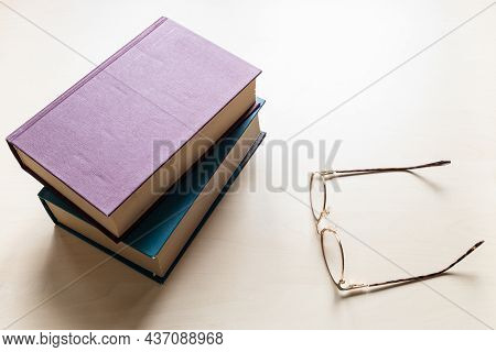 Top View Of Eyeglasses And Two Thick Volumes Of Books On Light Brown Wooden Board