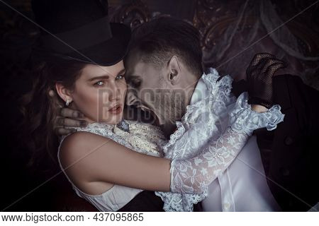Handsome bloodthirsty male vampire going to bite an innocent beautiful waman in his arms. Dark vintage castle background. Halloween. Vampires of the 19th century. 