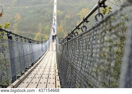 Suspension Wooden Bridge With Steel Ropes Over A Dense Forest In West Germany, Visible Tourists On T