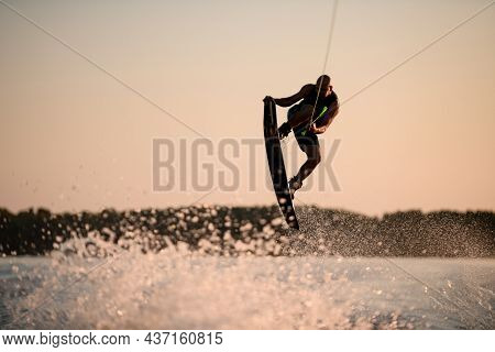 Muscular Man Making Trick In Jump Time With Wakeboard Against The Backdrop Of The Sky
