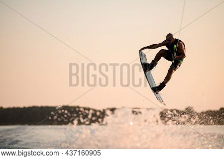 Energy Muscular Man Making Trick In Jump Time With Wakeboard Against The Backdrop Of The Sky