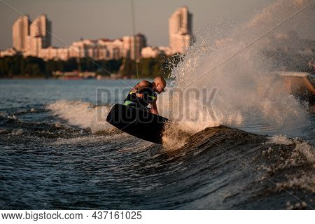 Athletic Guy Holds Rope And Speedly Riding Wakeboard And Trying To Stand On Splashing Wave.