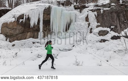 Winter run sport woman running on snow trail training cardio outdoors on cold weather. Asian runner girl working out outside wearing leggings and active coat.