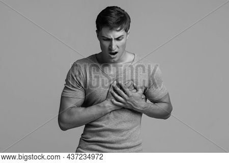 Sad Shocked Despaired Handsome Millennial Caucasian Male Suffering From Chest Pain, Pressing Hand To
