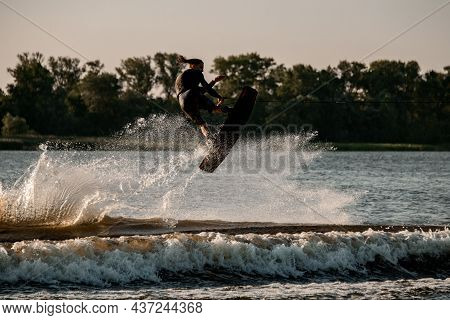 Great View Of Dynamic Guy Holding Rope And Jumping High With Wakeboard Over Water