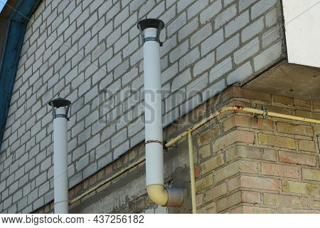 Two White Metal Chimney Pipes On A Brick Wall Of A House On The Street