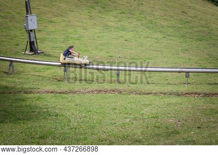 Bled, Slovenia - June 12, 2021: Boy, A Kid, Going Down A Slope Of Straza Bled With A Bobsled On A Su