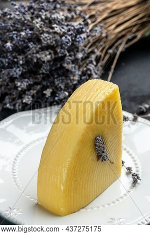 A Piece Of Cheese With Herbs On White Plate. Avender Cheese With Dry Basil And Lavender Flowers. Ver