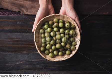 Wild Indian Gooseberry Or Amla In A Bamboo Basket Holding By Hand On Wooden Background, Fruit Tree I