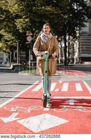 traffic, city transport and people concept - woman riding electric scooter along red bike lane with signs of bicycles and two way arrows on street