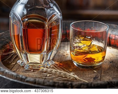 Carafe of whisky and glass of whisky on old wooden cask at the dark background.