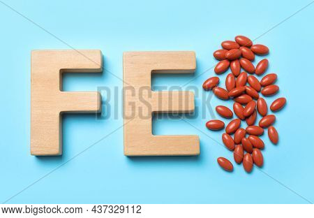 Wooden Letters Fe And Pills On Light Blue Background, Flat Lay. Anemia Treatment