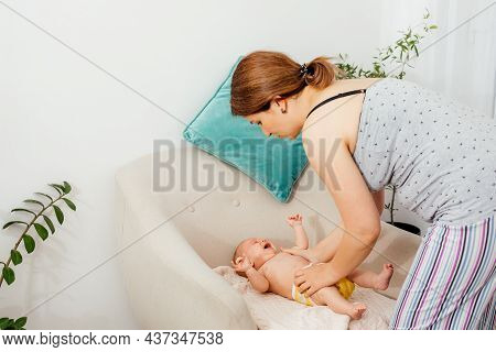 Mother Putting Clothes On Her Newborn Baby On The Chair