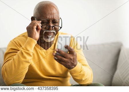 Black Man Using Smartphone Wearing Eyeglasses Having Poor Eyesight Indoor