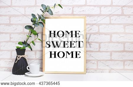 On A White Table Against A Light Brick Wall, A Branch Of Eucalyptus In A Dark Vase, A White Cup And 