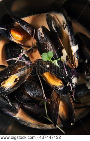 Mussel stew pot with creamy sauce, baguette on stone table. Mussels soup pot contemporary style. Aesthetic composition with seafood. Gastronomy mussel pot dinner concept. Stone table and wooden tray