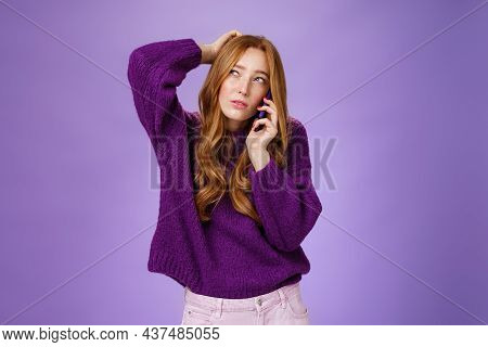 Confused Cute Redhead Female Making Appoinment Via Mobile Phone Scratching Back Of Head And Squintin