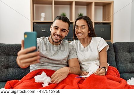 Young latin ill couple having medical teleconsultation using smartphone at home.