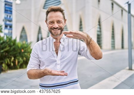 Middle age man outdoor at the city gesturing with hands showing big and large size sign, measure symbol. smiling looking at the camera. measuring concept. 