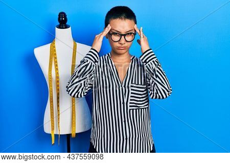 Beautiful hispanic woman with short hair standing by manikin suffering from headache desperate and stressed because pain and migraine. hands on head. 
