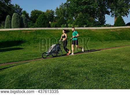 Running Sports Couple Pushing Jogging Stroller With Child In Park At Outdoors. Morning Run For A Who