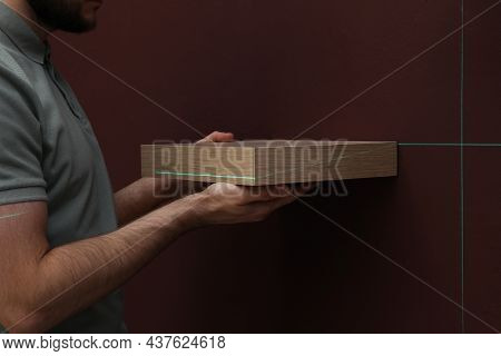 Man Using Cross Line Laser Level For Hanging Shelf On Brown Wall, Closeup
