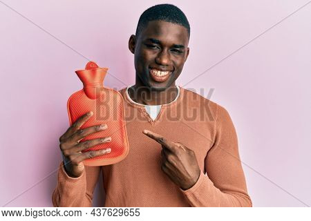 Young african american man holding heat water bag smiling happy pointing with hand and finger 