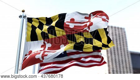 The Flag Of The Us State Of Maryland Waving In The Wind With The American Flag Blurred In The Backgr