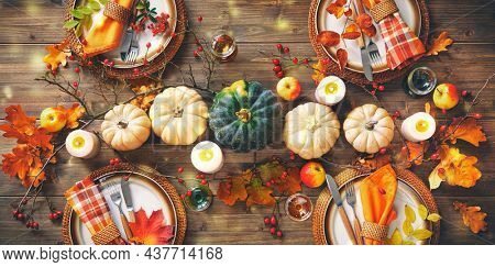 Autumnal decorated table for celebrating Thanksgiving or other family celebration. Festive table setting with plates, glassware, pumpkins, rose hip branches and leaves on wooden table background