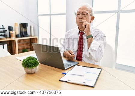 Senior man working at the office using computer laptop mouth and lips shut as zip with fingers. secret and silent, taboo talking 
