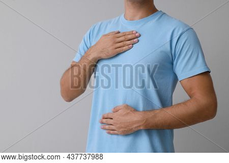 Man Holding Hands Near Chest On Grey Background, Closeup. Space For Text