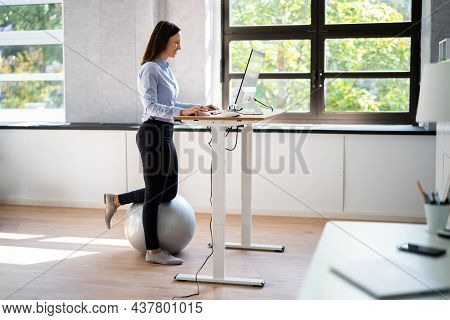 Woman Using Adjustable Height Standing Desk In Office For Good Posture