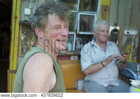 An Adult Son Laughs Merrily Against The Background Of An Elderly Old Man's Father. Father And Son.