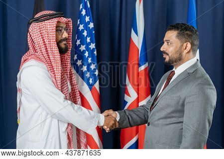 Confident middle easterns political leader in ghutrah handshaking with other country representative while they making alliance